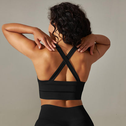 Woman wearing a black sports bra with criss-cross straps on a neutral background